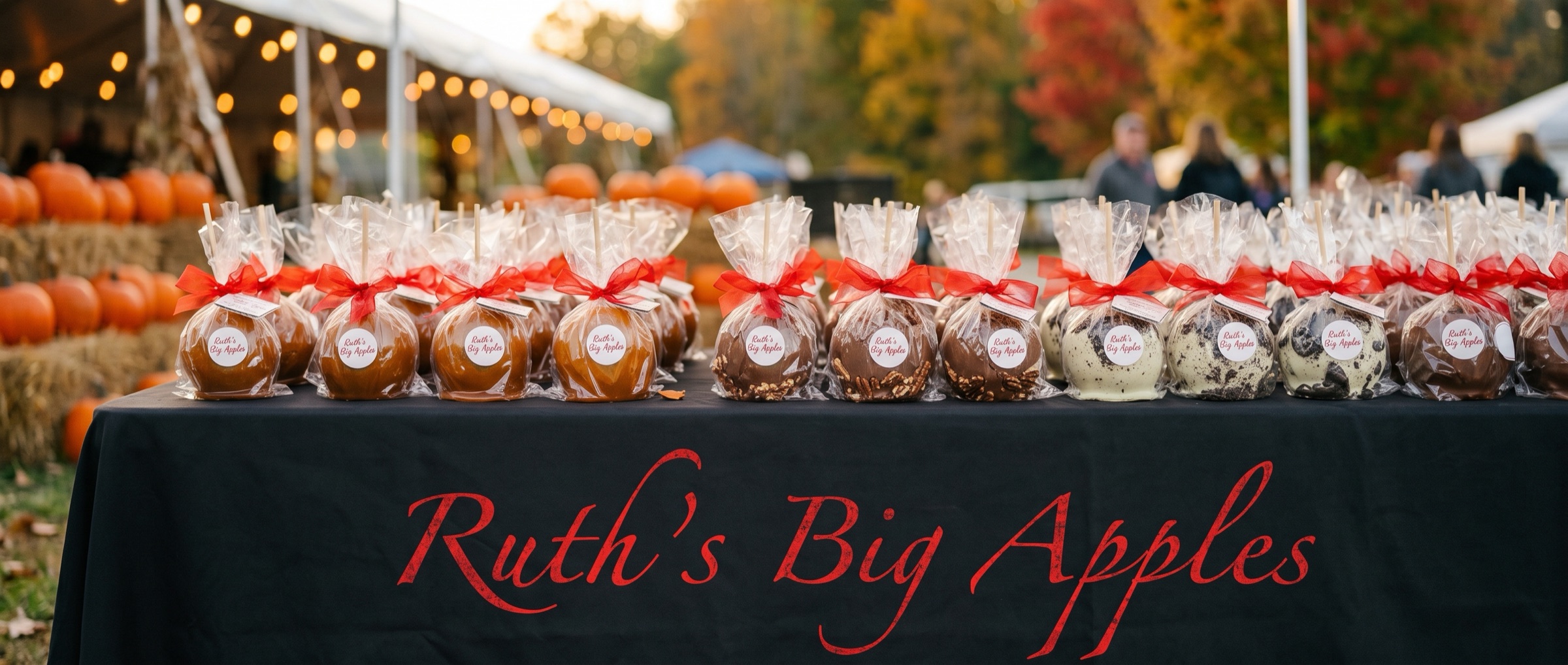 Rows of candy apples wrapped in cellophane and tied with red bows on a black tablecloth printed with Ruth's Big Apples, at an autumn festival