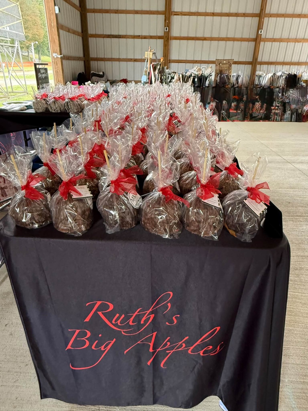 Rows of candy apples in clear cellophane tied with red bows on a black tablecloth printed with Ruth's Big Apples