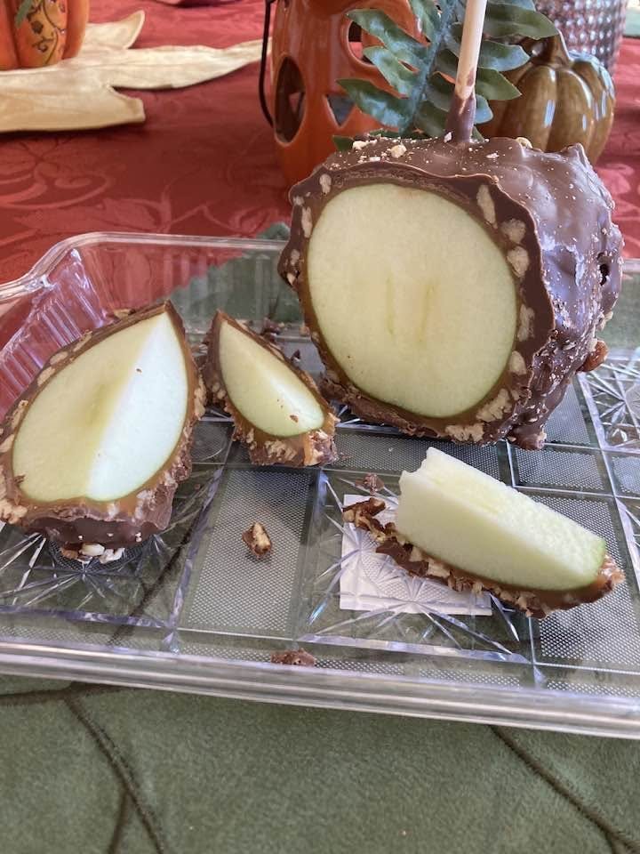 A chocolate caramel apple sliced open to show a thick layer of caramel around a crisp green apple
